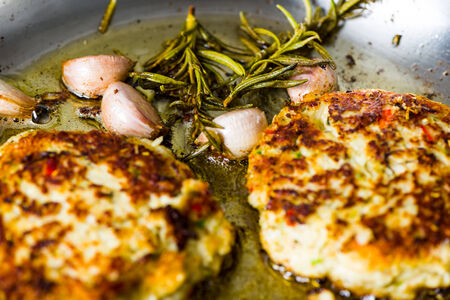 two fresh fried rissole in a pan with garlic and rosemary