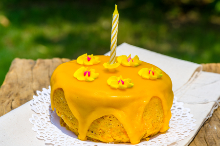 Striking yellow sponge cake topped with melted fondant with six jelly flower candies and candle for one year oldの写真素材