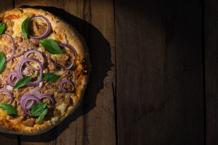 top view of a round tuna pizza with onion rings on a dark wooden tableの写真素材
