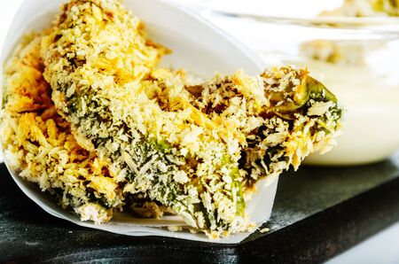 breaded baked avocado pieces served with a mayonnaise sauce on dark wood plate and white backgroundの写真素材