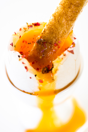 Soft boiled egg in eggcup with pepper and slice of toasted toast isolated on white backgroundの写真素材