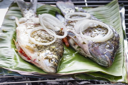 Freshly prepared fish on barbecue with vegetables and lemon. The fish is on banana leafの写真素材