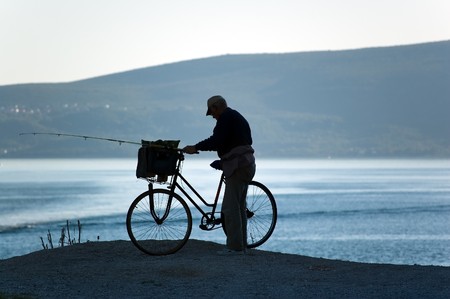 Fisherman silhouette with the bike. Sea bay and hills in the background, summertimeの写真素材