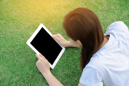 Young woman lying on grass using tabletの写真素材