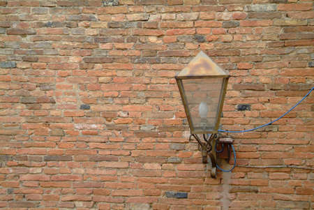 rusty old lamp on red brickswall with a blue cableの写真素材