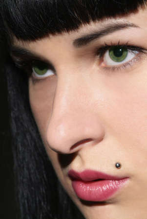 face of a black haired woman with green eye and piercingの写真素材