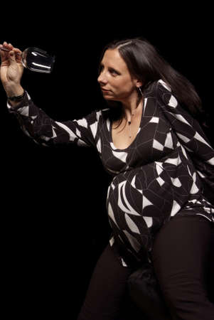 pregnant woman looks serious at empty wine glassの写真素材