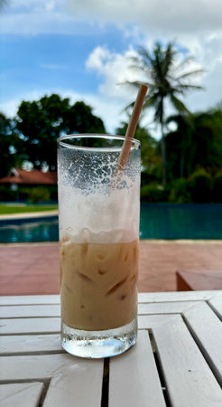 Iced coffee in a tall glass on the table near the swimming pool