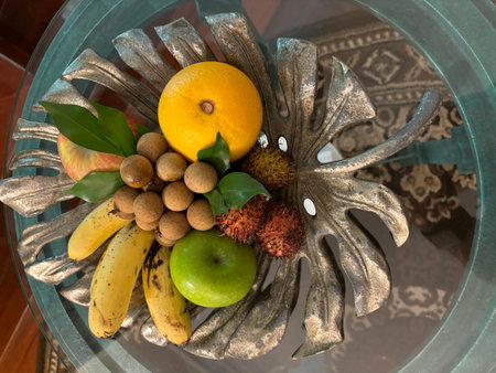 Tropical fruits in a glass vase on a wooden tableの写真素材