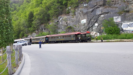 Passenger train moves along the road in the mountains in the summerの写真素材