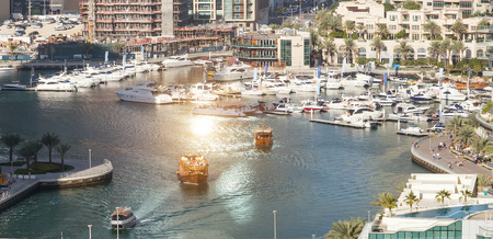 panoramic view of skyscrapers hotel and water pier of Dubai Marina at sunrise.