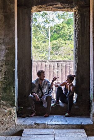SIEM REAP, CAMBODIA - March 01, 2015: Young girl and man friendship tourist sit doorway in the ancient ruins temple in Angkor Archeological area in Cambodiaのeditorial素材