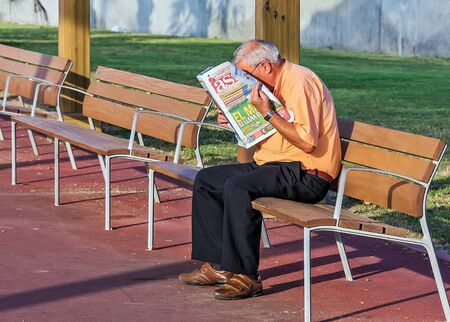 BARCELONA, SPAIN - August 22, 2012: Grandfather pensioner sit outdoors in park, senior man reading the latest news Newspaper.のeditorial素材