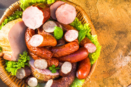 Various meat and sausage in a basket on a wooden tableの写真素材