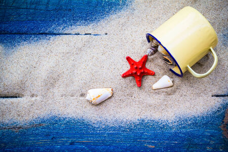 Colorful shells in a cup on the sand strewn on blue boardsの写真素材