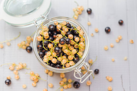 Fruits black and white currants in a jar on a wooden tableの写真素材