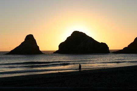 a sunset over the ocean with a silhouette of the rocksの写真素材