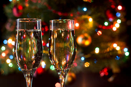 two glasses with champagne and candles on the background of the Christmas tree with garlandsの写真素材