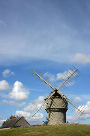 a historic french windmill photographed in the summer sun with blue and cloudy sky in the backgroundの写真素材