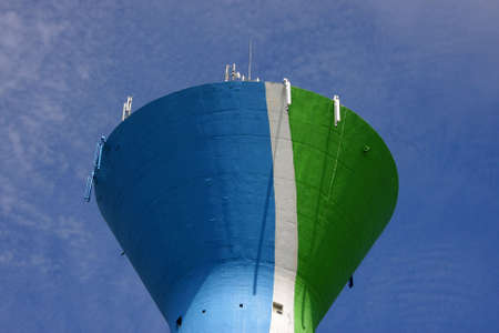 a colourful water tower, painted in blue, green and white, with cellular phone network antennas on...