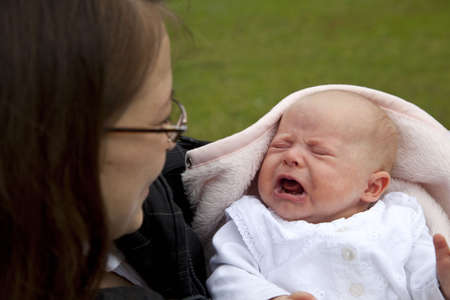 A happy, smiling and proud young mother holding her 7 weeks old crying daughter の写真素材