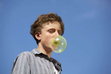 A thirteen years old teenager making fun with blowing a huge chewing gum bubbleの写真素材