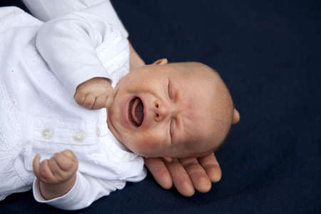 A crying 7 weeks old baby girl with her head held by her fathers hand over a blue blanketの写真素材