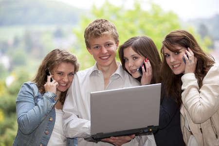 Four happy smiling and laughing teenagers with cellphones and a laptop