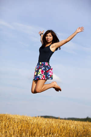 a happy and jumping brunette teenage girl photographed during late evening sun on an acreの写真素材
