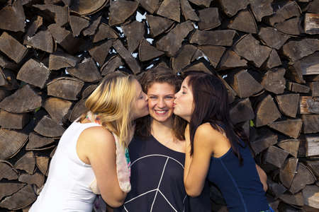 two teenage girls kissing their laughing girl friend in the middle on her cheeksの写真素材