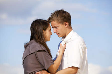 A teenage couple standing head to head and having a dispute, photographed with blue sky and clouds...
