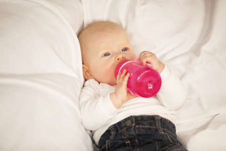 A relaxed eight months old baby girl lying on a couch and drinking from her baby bottleの写真素材