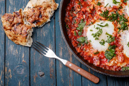 Fried eggs in a frying pan with tomatoes, sausage and greens.の写真素材