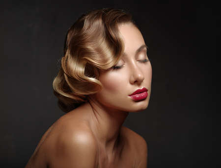 Portrait of a beautiful girl on a dark background. Closed eyes. Red lips and nails. Wavy hairstyle.の写真素材