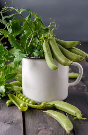 Heap of young green peas whole and broken with leaves and flower in vintage cup over old wooden table. Dark rustic style.の写真素材