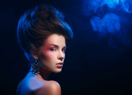 Dramatic portrait of a beautiful girl with earrings. Woman half-turned, looking at the camera. High fashionable hairstyle.の写真素材