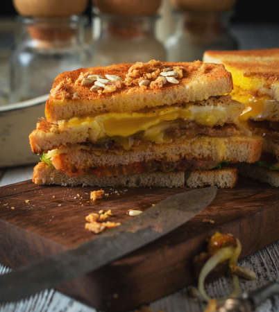 Sandwich with egg, tomato, onions and bacon on a vintage wooden background in rustic style. Toned.