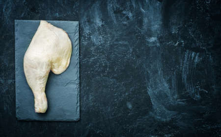 Raw chicken thigh on black stone plate. Copyspace.の写真素材