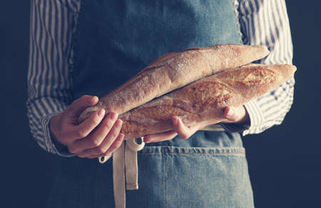 Baker's hands hold fresh baguettes.