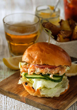 Fishburger with toppings, fries  and a glass of beer. Rustic style.の写真素材