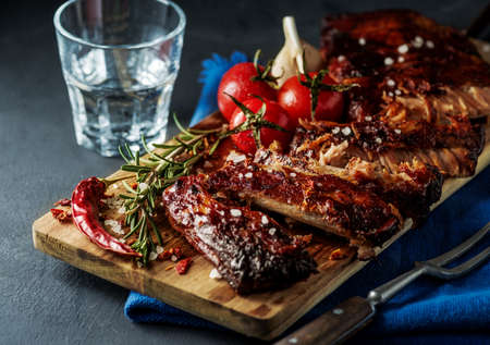 Delicious barbecued ribs seasoned with a spicy basting sauce and served with chopped fresh vegetables on an old rustic wooden chopping board in a country kitchenの写真素材