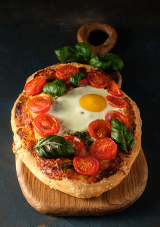 Homemade tasty pizza with egg, cheese, tomatoes and basilの写真素材