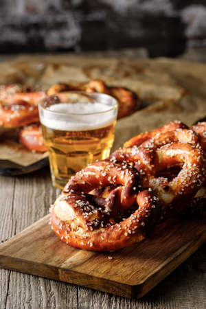 Freshly baked homemade soft pretzel with salt on rustic wooden table with glass of beer.の写真素材