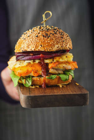 Chicken burger with pineapple. Men's hands hold a tray with a cheeseburger.の写真素材
