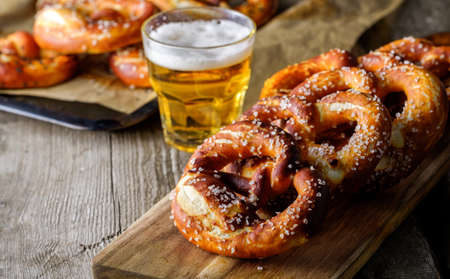 Freshly baked homemade soft pretzel with salt on rustic wooden table with glass of beer.