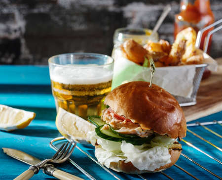 Fishburger with toppings, fries  and a glass of beer. Rustic style.の写真素材