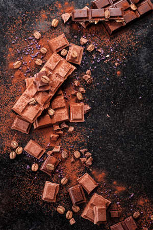 Broken chocolate pieces and cocoa powder on marble. The chunks of chocolate over dark background