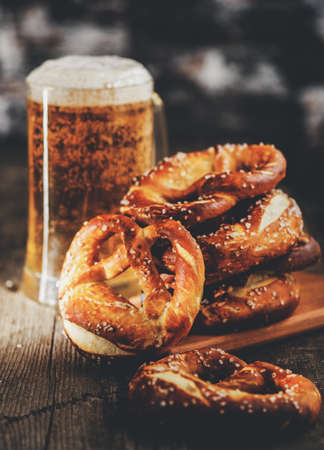 Freshly baked homemade soft pretzel with salt on rustic wooden table with glass of beer.の写真素材