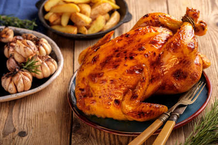 Roasted chicken  in a plate on a wooden table with garlic and potatoesの写真素材