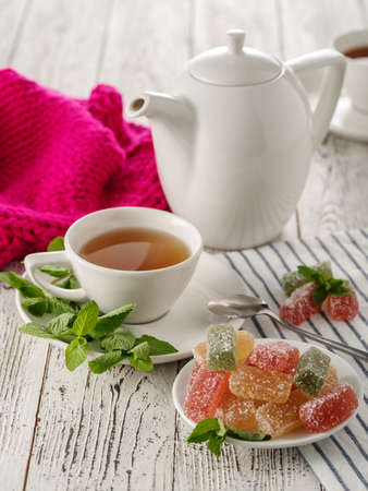 Tea drinking. White kettle with a cup of tea with marmalade and mint on a white wooden tableの写真素材